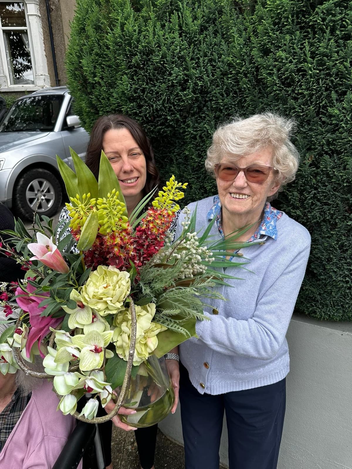 A smiling resident holding a large bouquet of flowers outside, with a member of staff