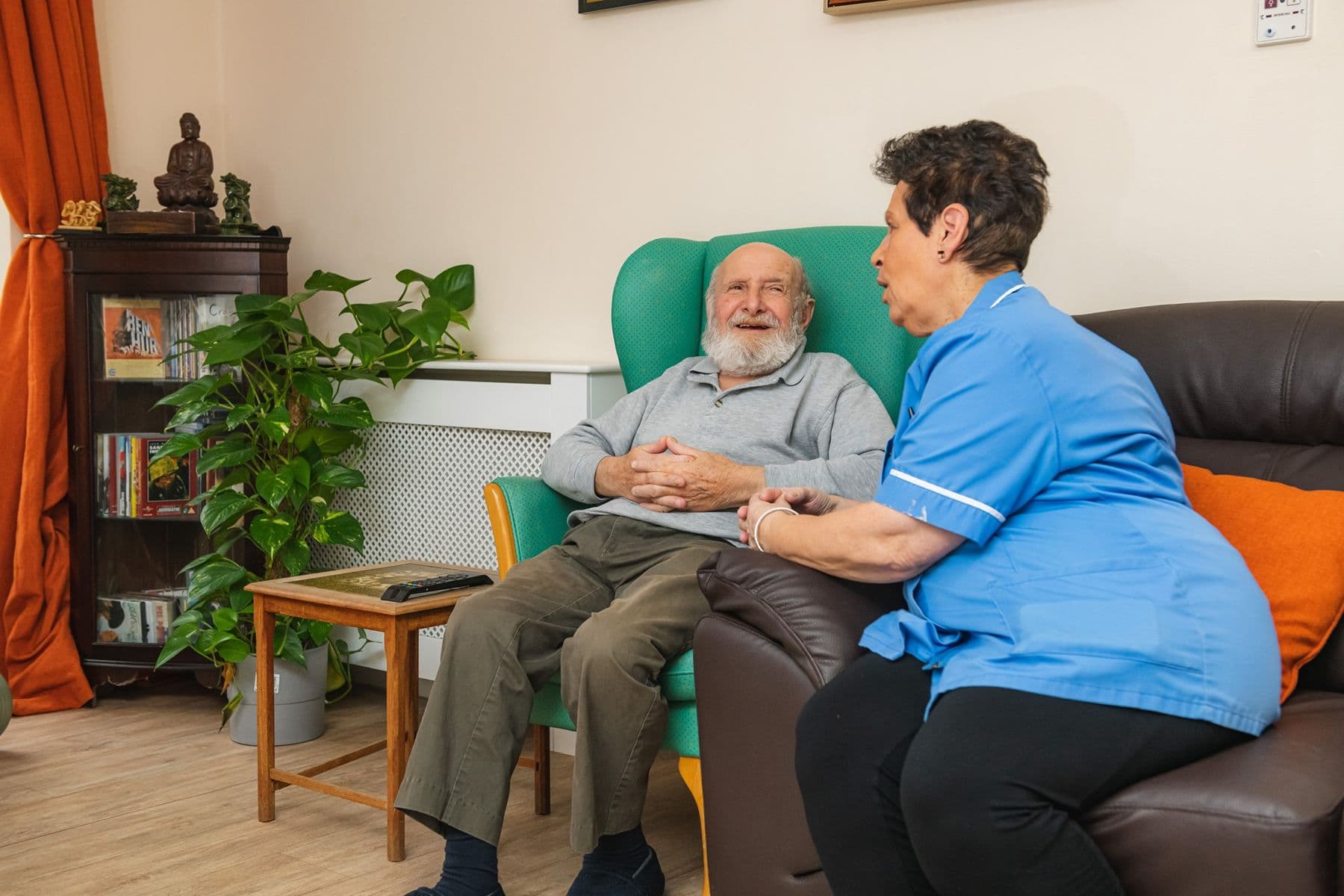 A resident relaxing in an armchair in the lounge, chatting with a carer